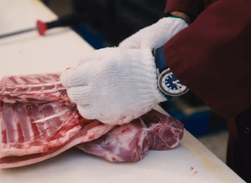 An Iasenza butcher in cut-resistant gloves trimming a cut at the counter
