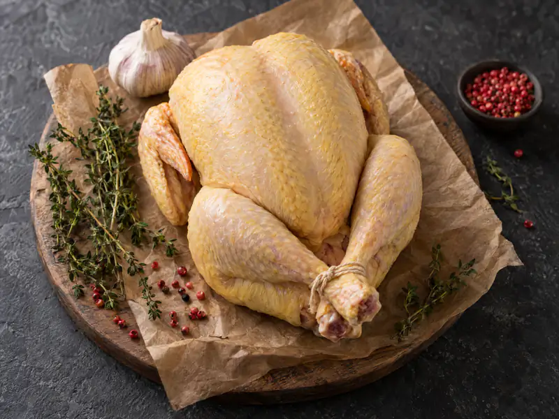 Raw whole grain-fed chicken, trussed, on a wooden board